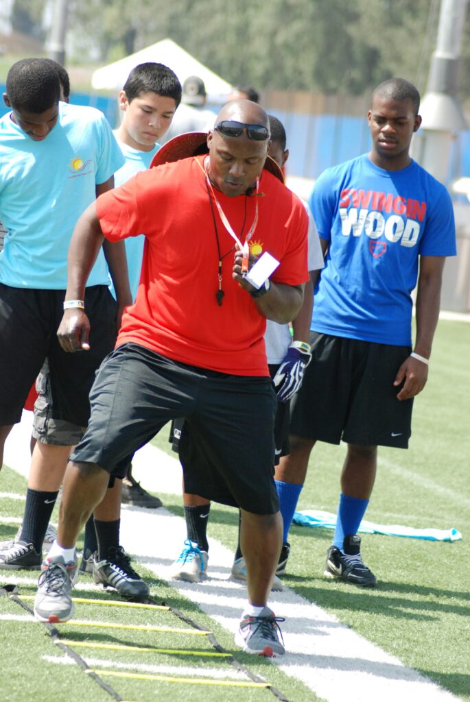 Coach Ty Pinkney demonstrating football agility drills to foster youth on the field.